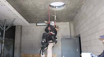 Man is harnessed with oxygen tank and coming through hole in ceiling